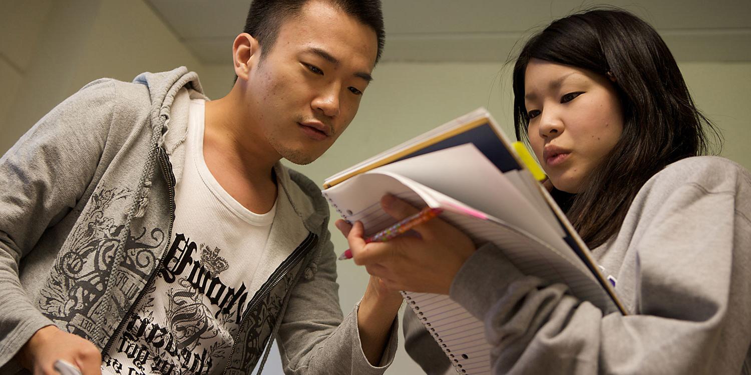 young man helping young woman holding a notebook and pen